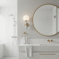 Modern bathroom with round mirror, white towels, and satin brass fixtures. Sconce concrete design.