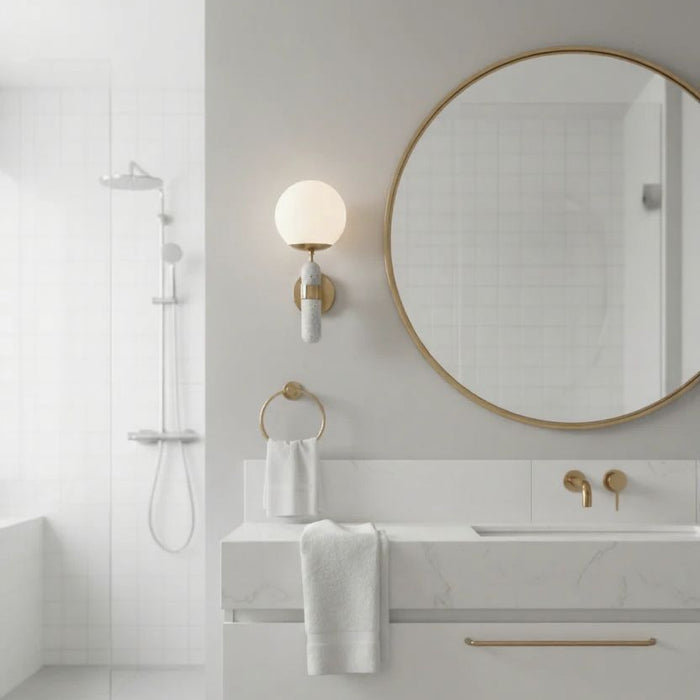 Modern bathroom with round mirror, white towels, and satin brass fixtures. Sconce concrete design.